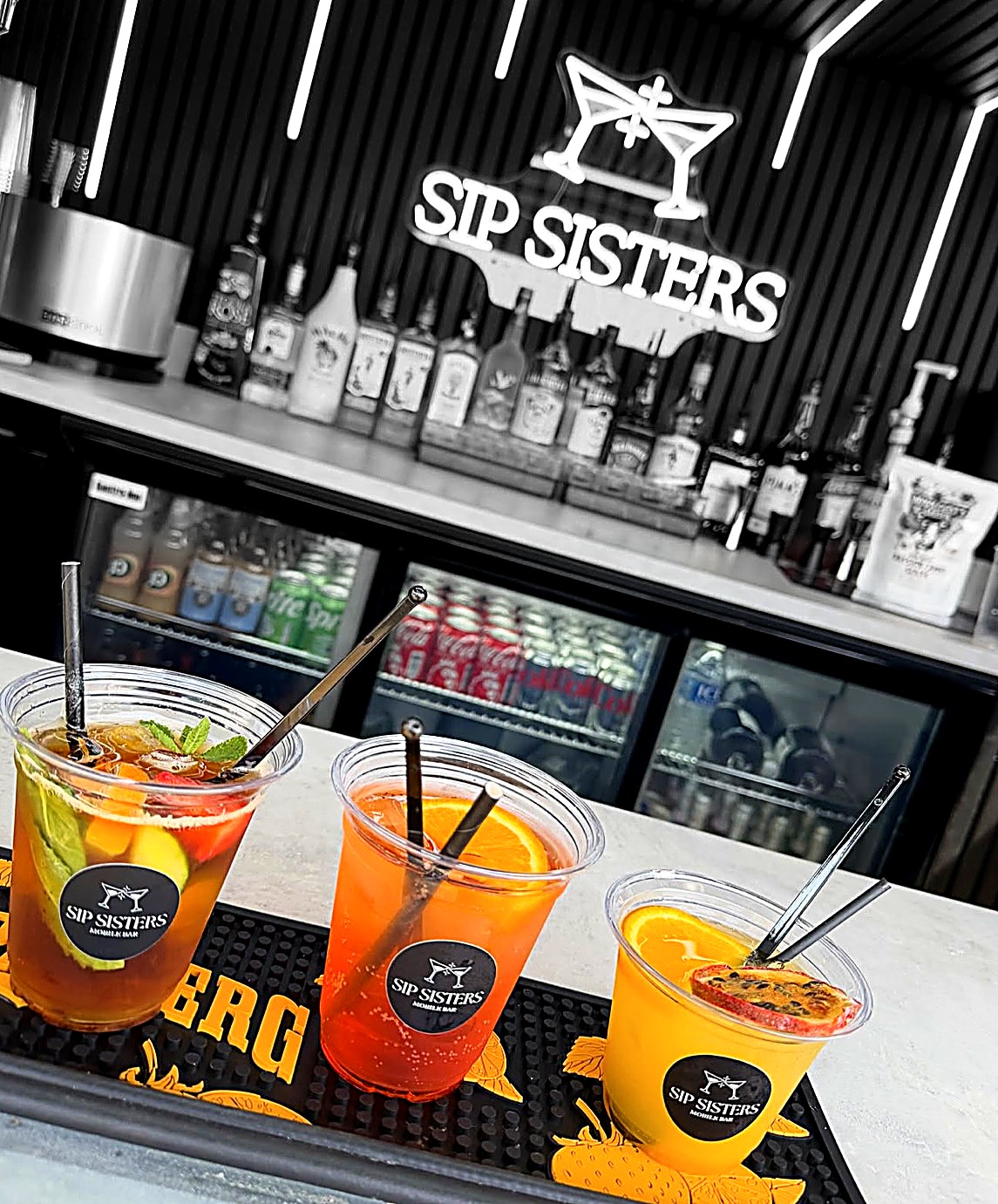 Three branded Sip Sisters cocktails on the bar with the neon sign behind