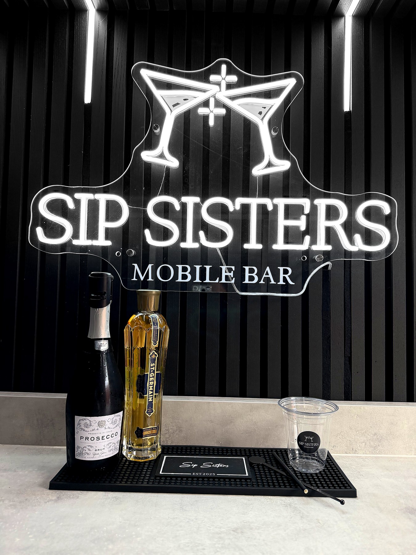 Sip Sisters neon sign with Prosecco and St-Germain on the bar